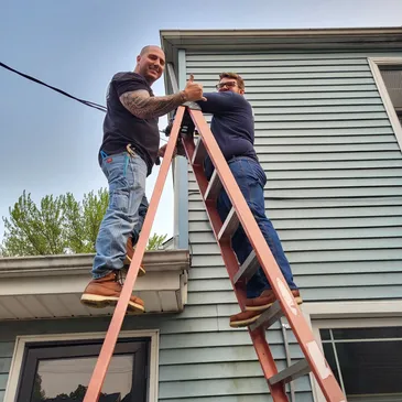 Two men on a ladder working on the side of a house.